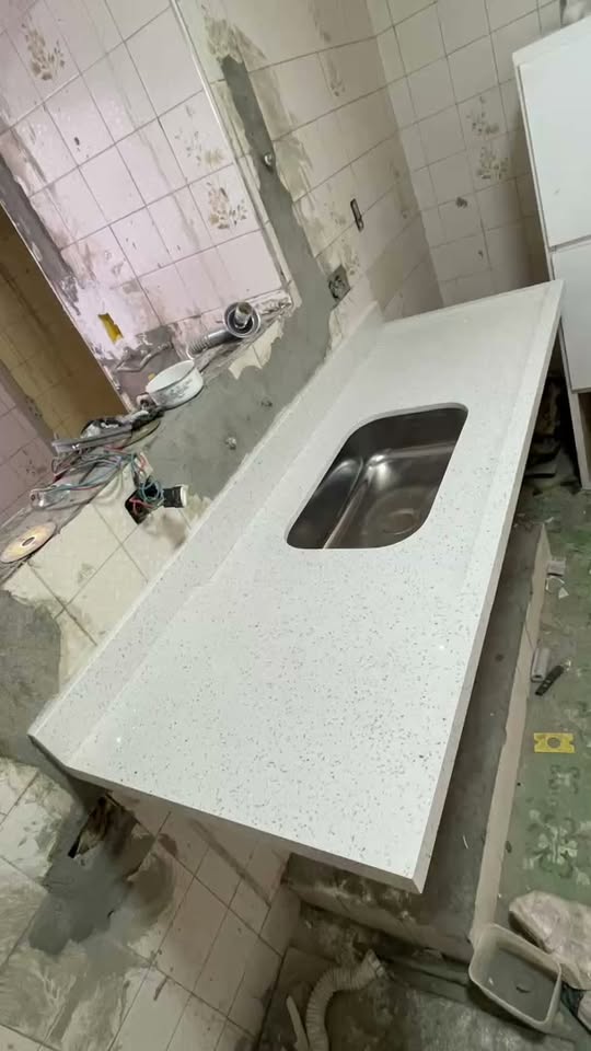 Bancada de cozinha em pedra clara com cuba de inox instalada